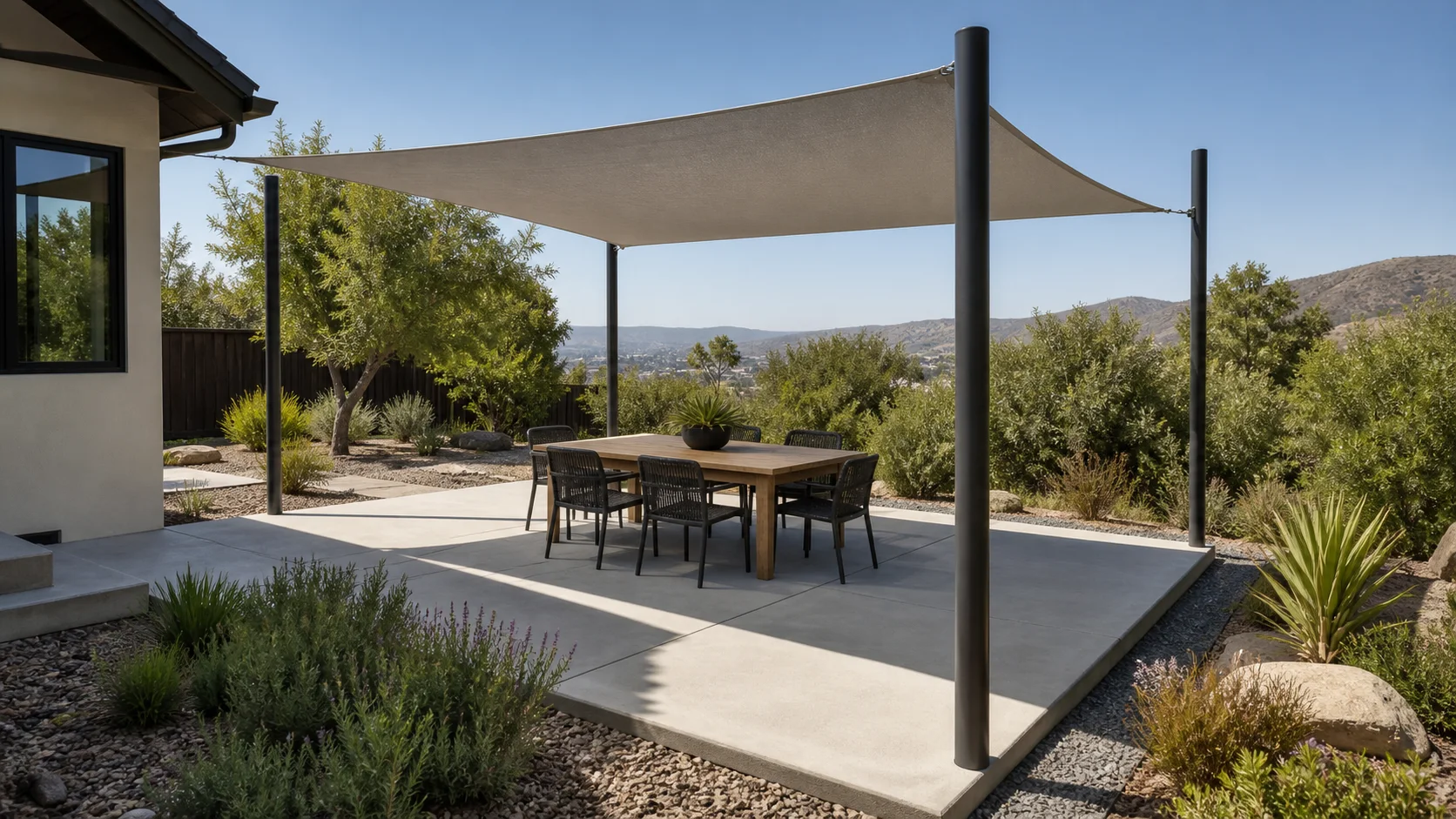 Minimal concrete patio with a tensioned shade sail over a compact outdoor dining area.